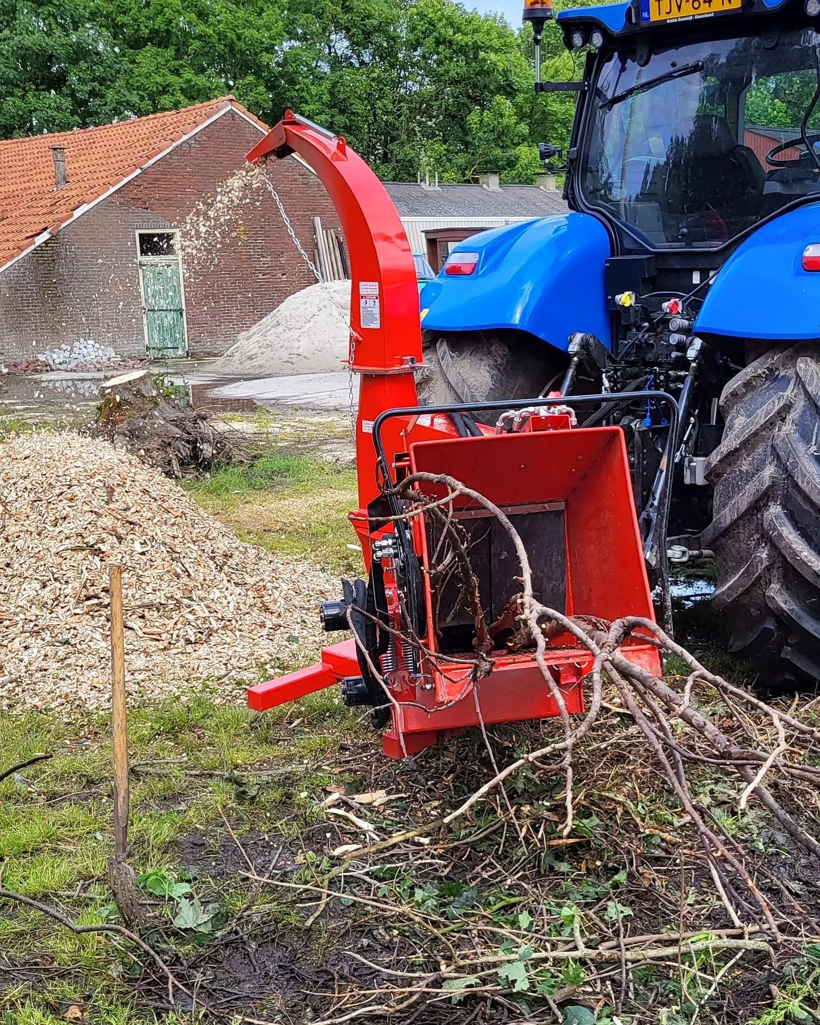 Rode houtversnipperaar achter de trekker met een hoop verse houtsnippers
