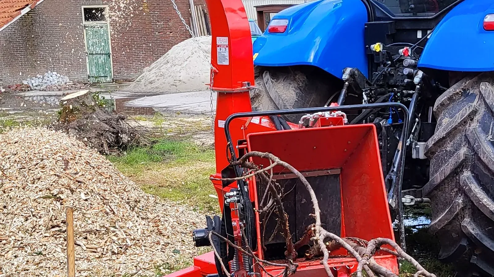 Rode houtversnipperaar achter de trekker met een hoop verse houtsnippers