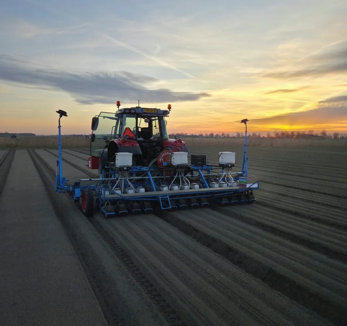 Tractor met zaaimachine op ruggen bij zonsondergang