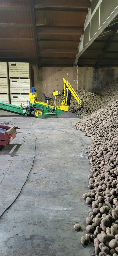 Groen-gele landbouwmachine naast opgeslagen aardappelen in een loods