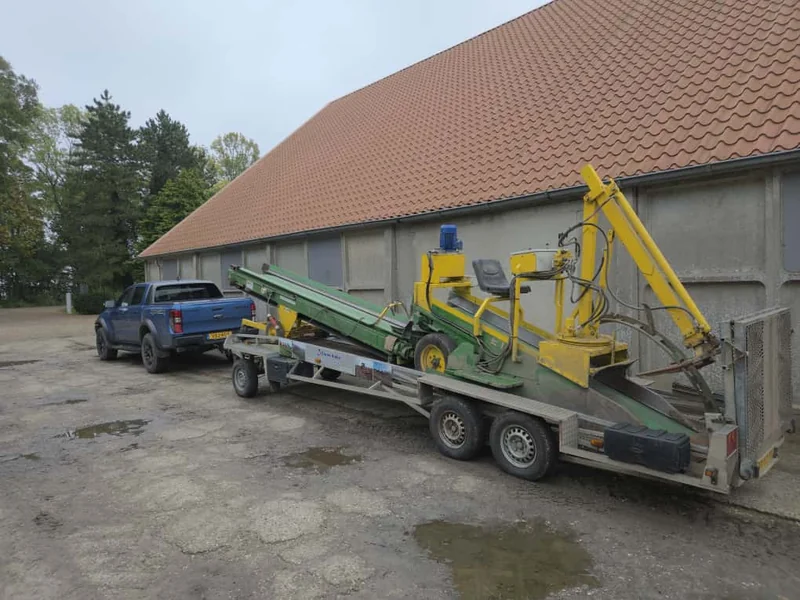 Groen-gele landbouwmachine op een aanhanger op het erf
