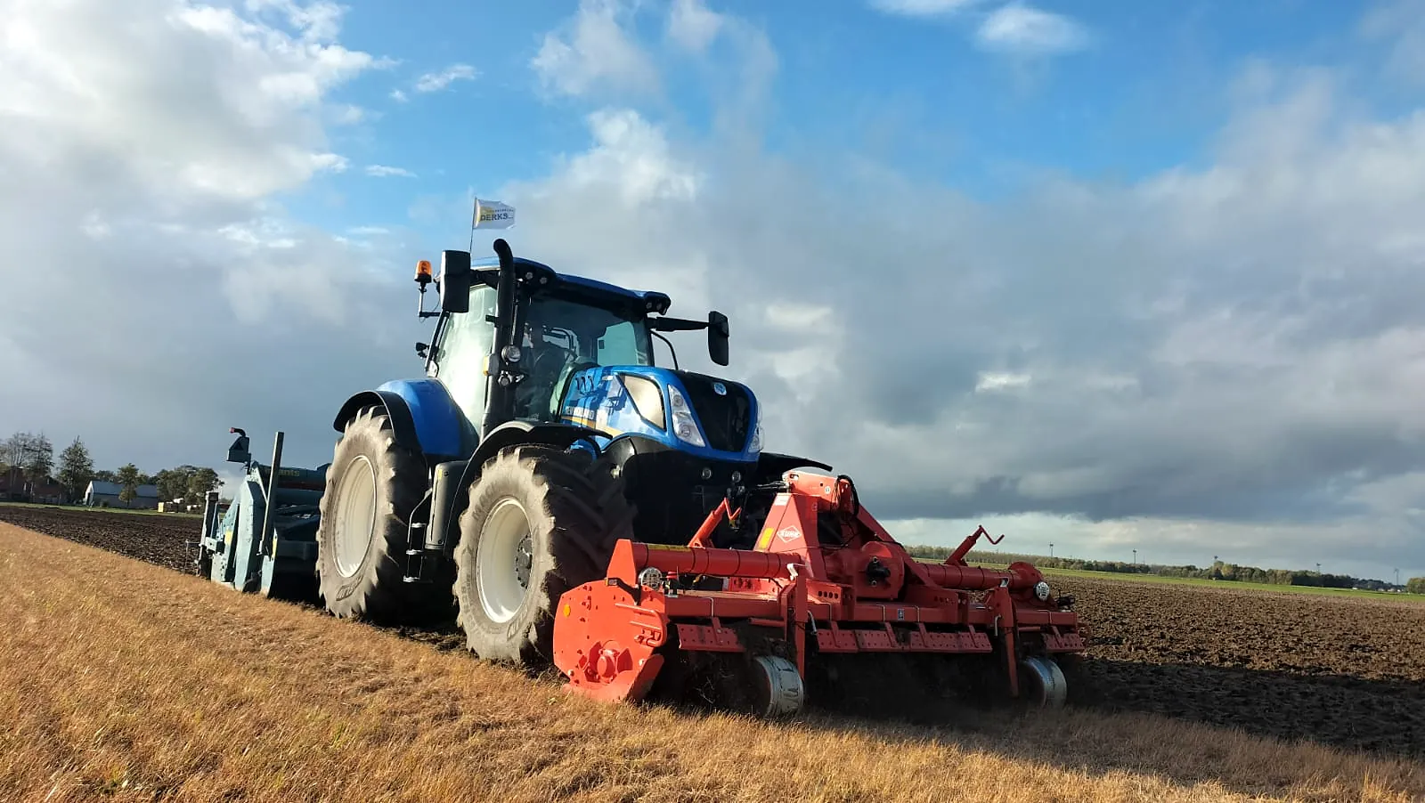 New Holland trekker met rode Kuhn frees aan het werk op een akker onder een wolkenlucht