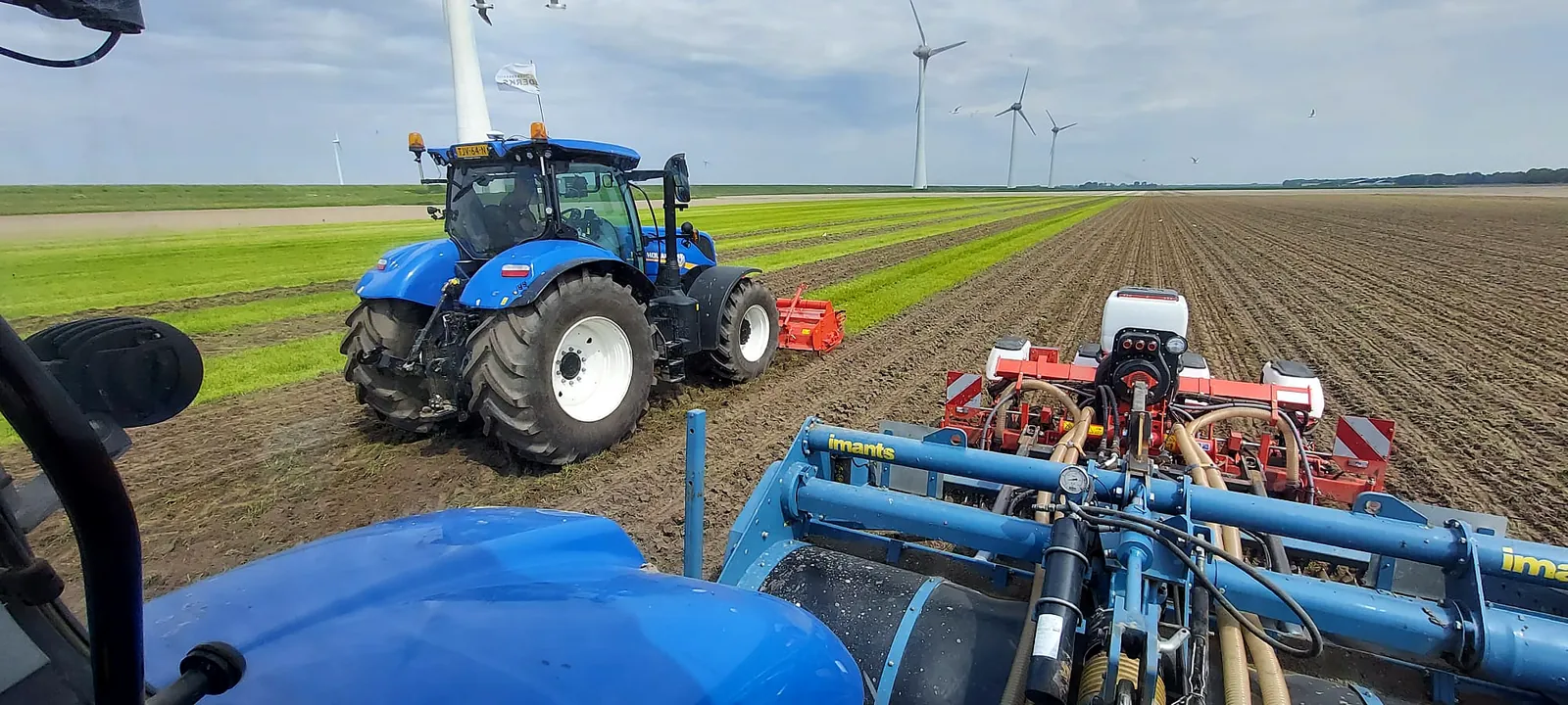 Uitzicht uit de cabine op de spitmachine en een tweede trekker op het perceel